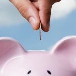 Male hand putting a coin into piggy bank