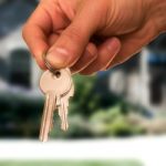 hand holding keys, house in the background