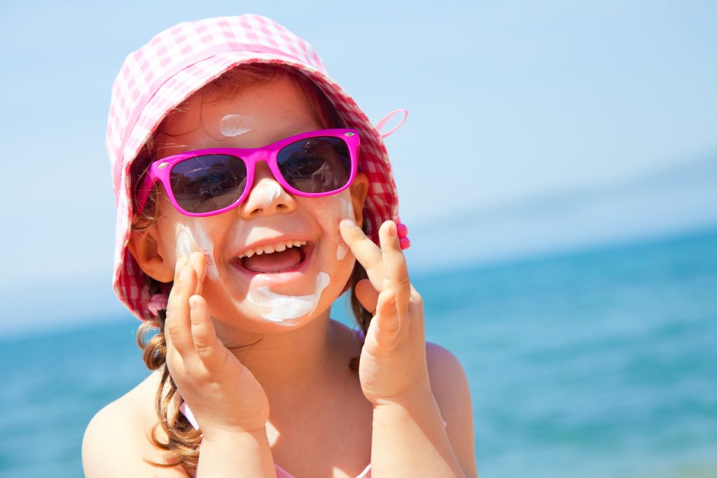 Girl anoints her face protective cream on the beach